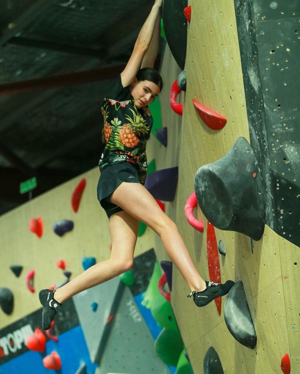 Tihana bouldering in a gym wearing a Wild Earth shirt