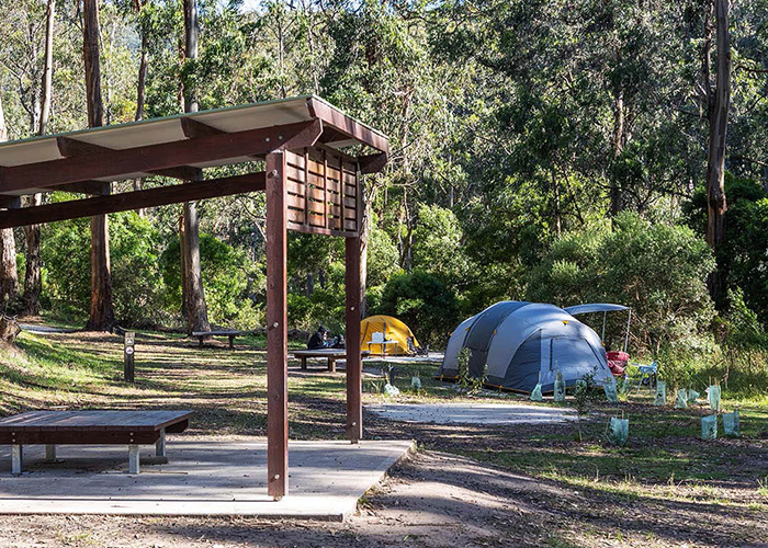 Tent camping amongst the trees with a wooden shelter nearby