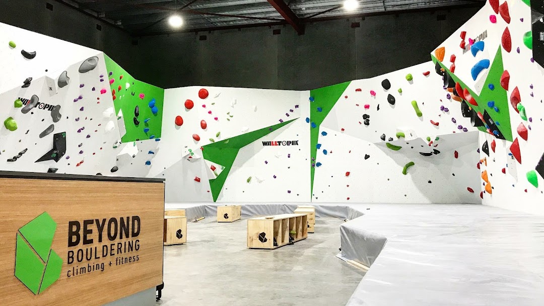 Bouldering gym with white walls and floor crash pads with green accents