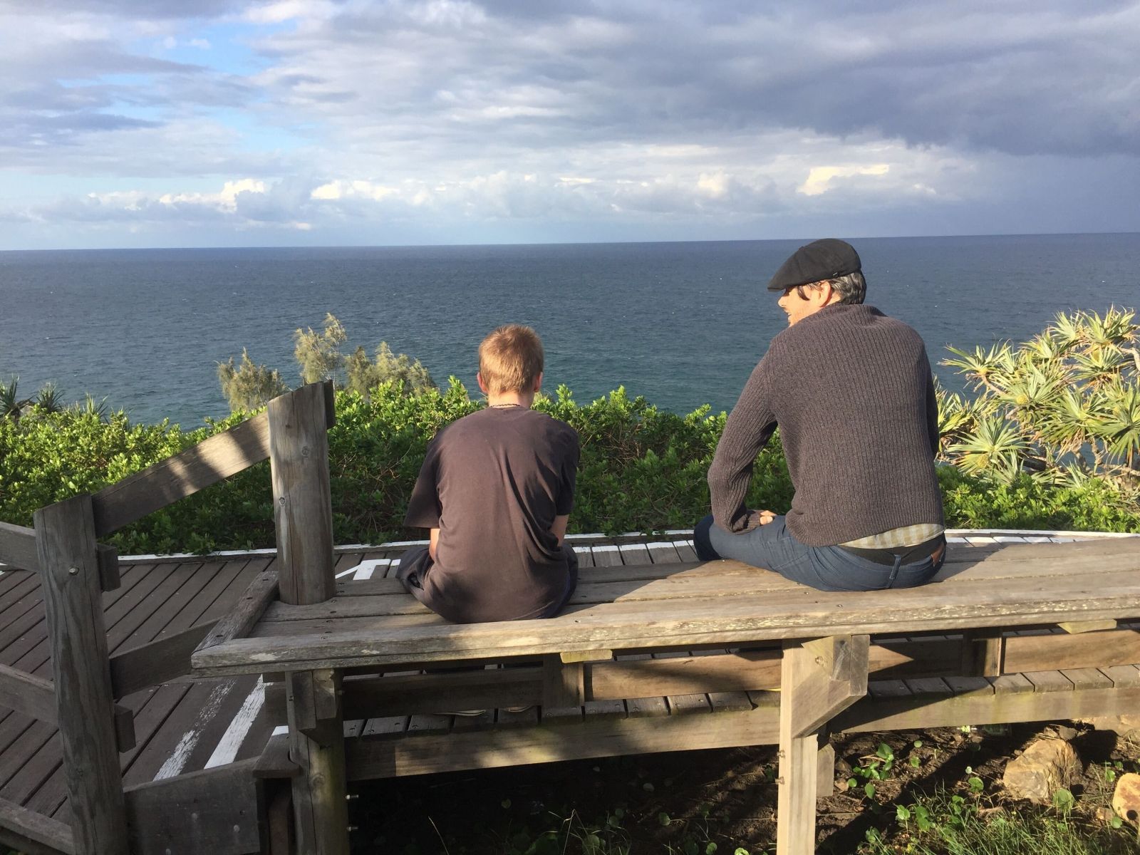 Man in his 40s speaking with a young boy on a seat by the ocean