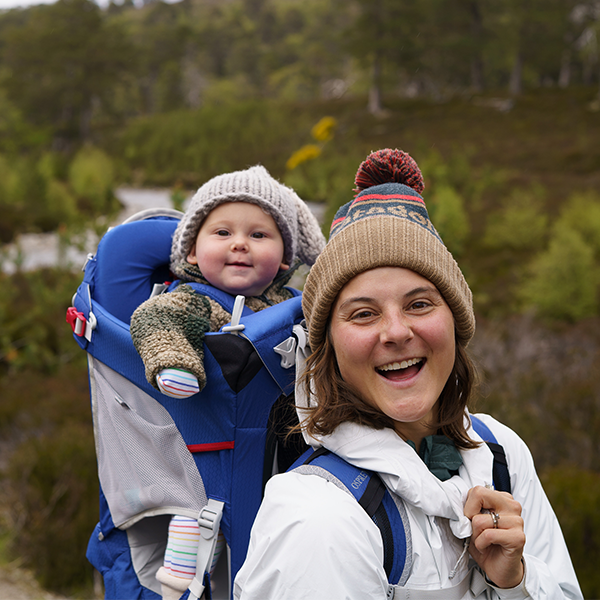 Emily with baby daughter on her back while wearing winter clothing and beanies