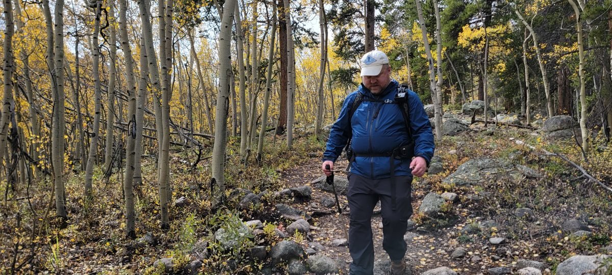 A man in hiking gear heading downhill on a forested trail