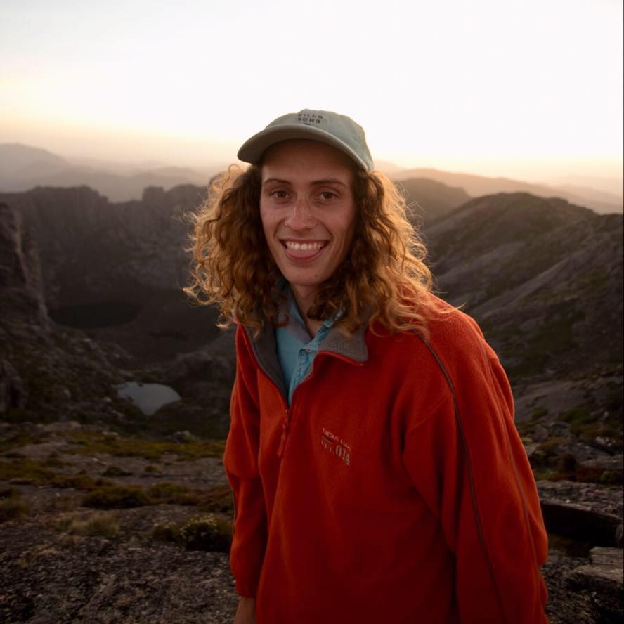 Man in his 20s/30s with curly hair wearing a hat and red jacket