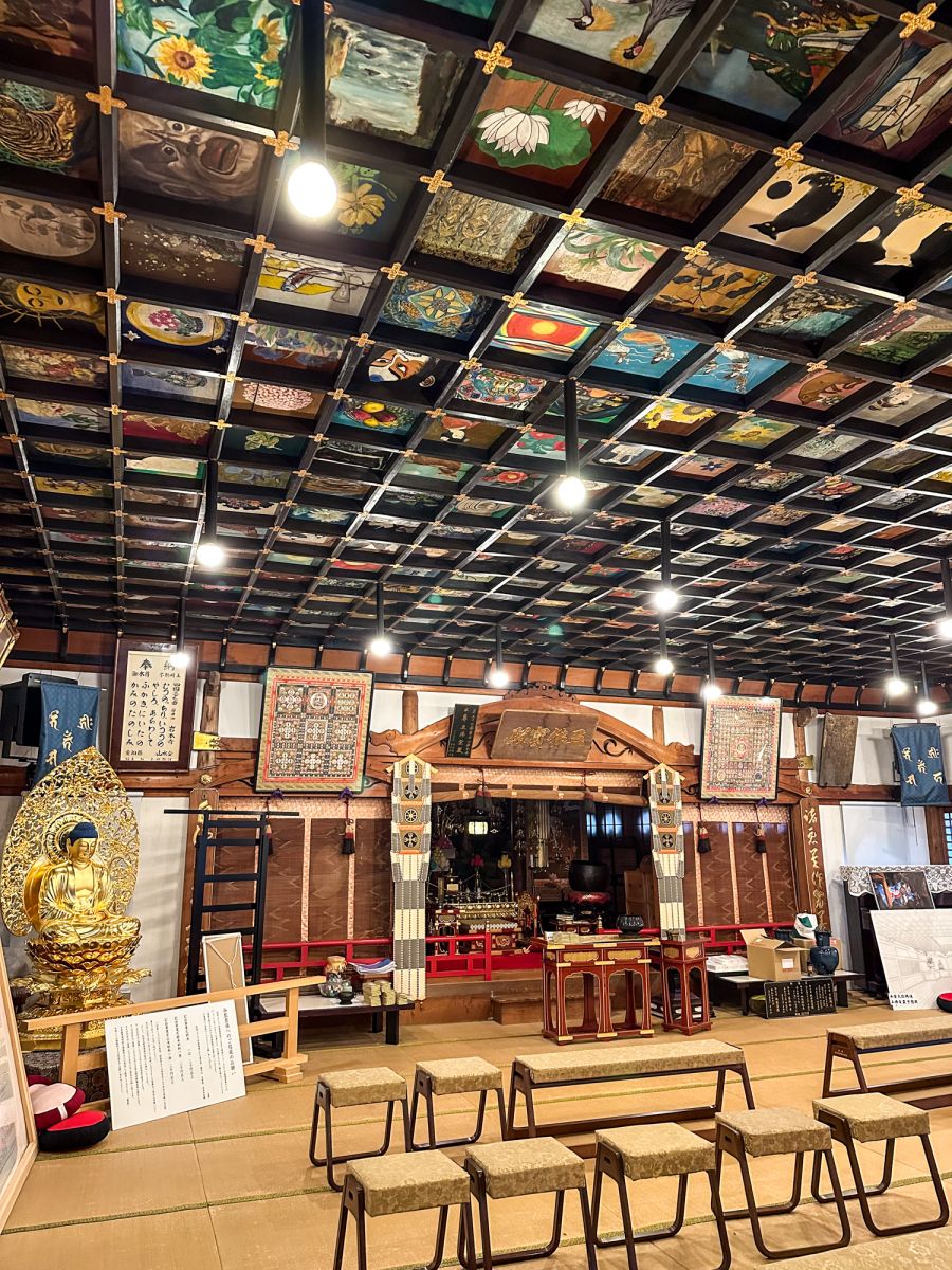 Inside Temple 37. The ceiling is divided into small wooden squares each with unique artwork including spirit's faces, flowers, fish and animals