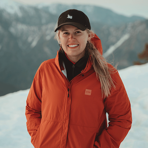 Jacinta Pink wearing an orange rain jacket on a mountain peak.