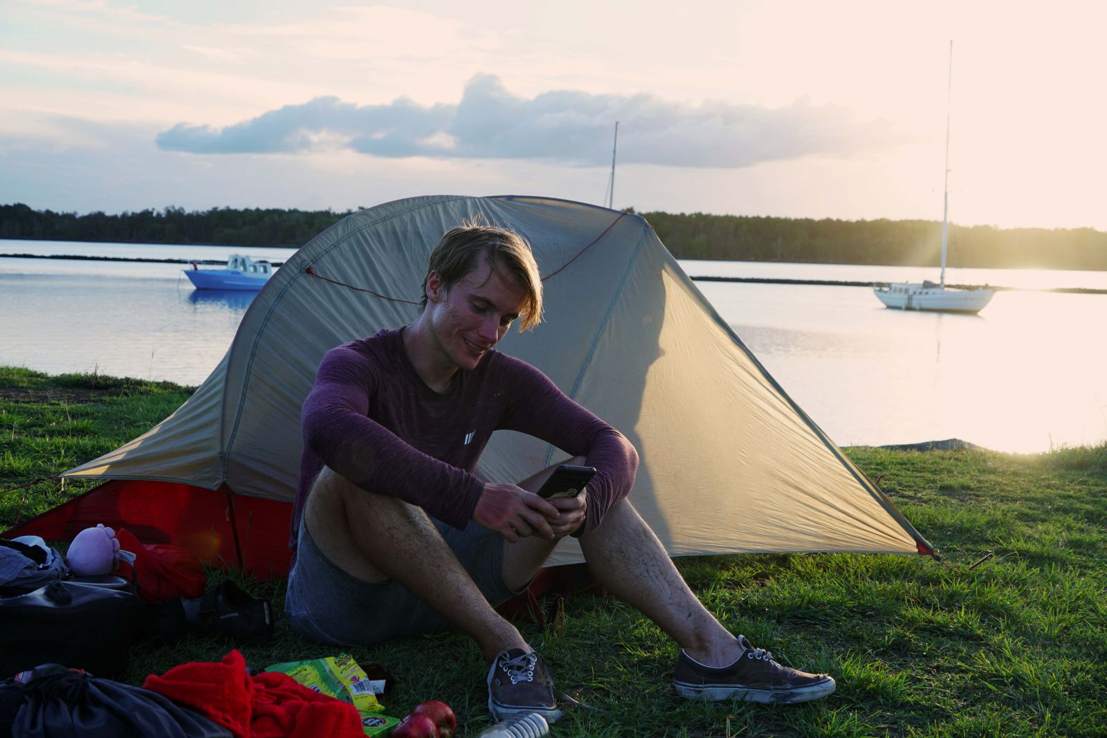 James sitting in front of their tent with the sun setting in the background over the coean