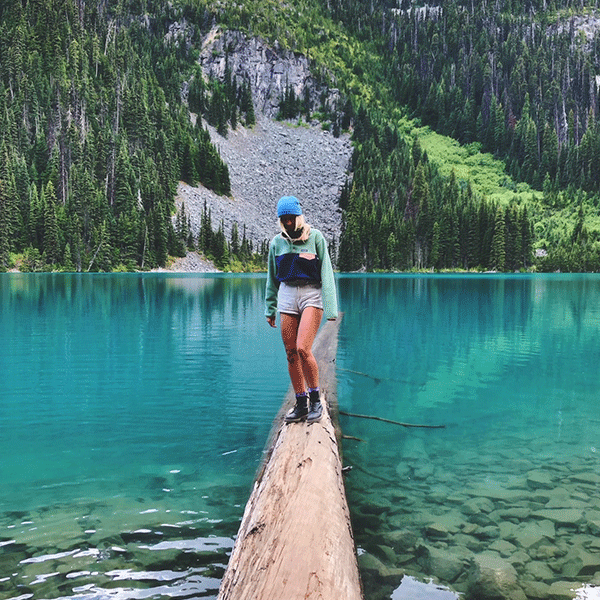 Jemma standing on a log in a lake with mountains in the background