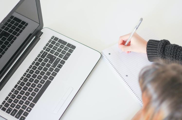 Woman making checklist using notebook and laptop