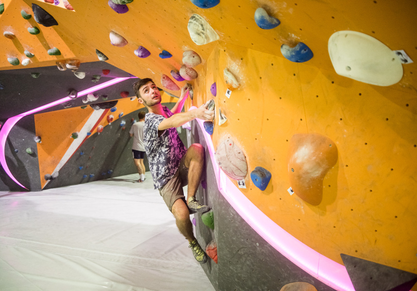 Man in his 20s climbing on an orange bouldering wall