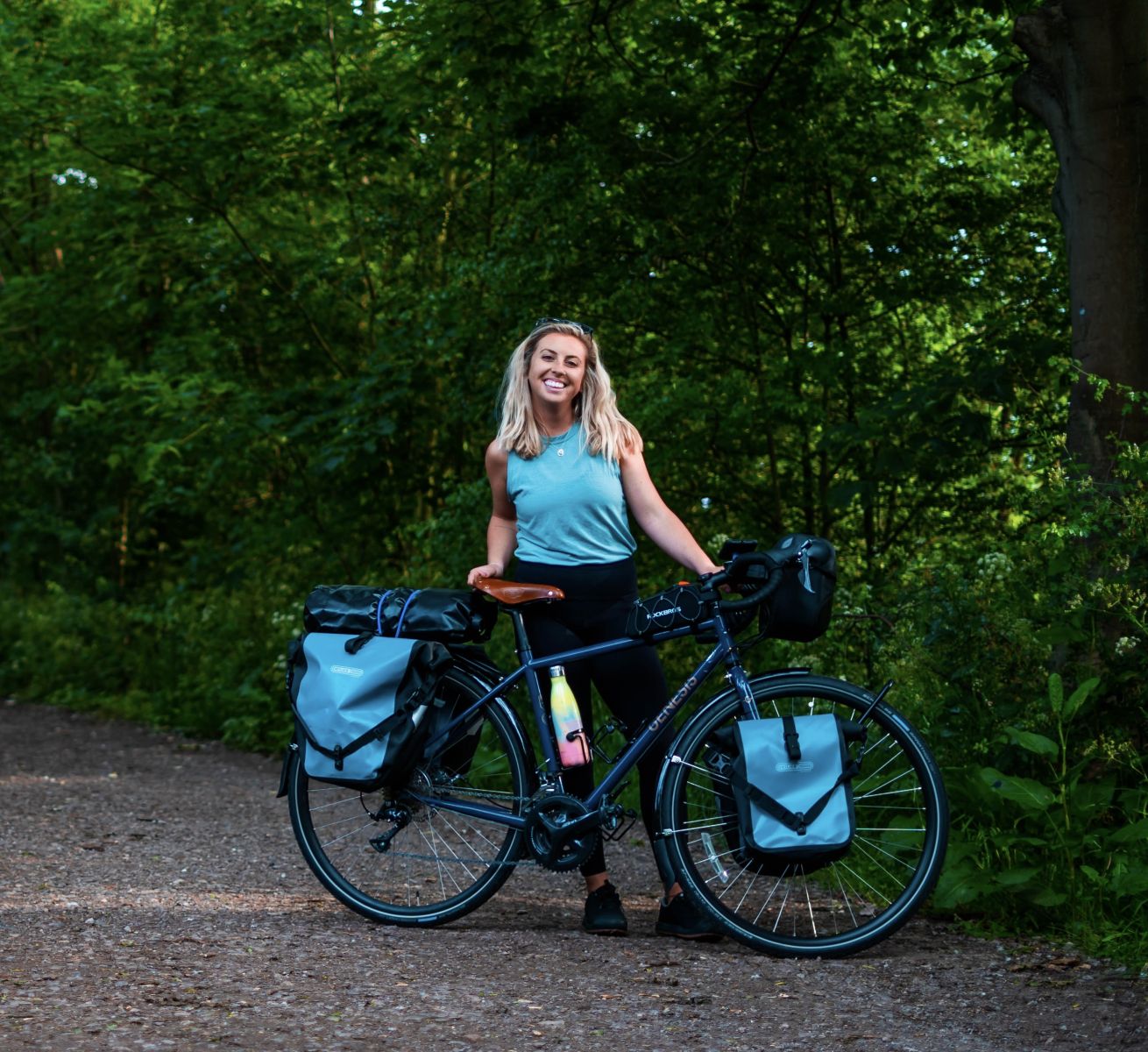 Woman in her late 20s wearing a blue top and black leggings standing with a bike