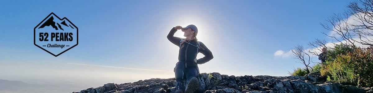 Hiker doing summit salute on top of peak with the 52 Peaks Challenge logo featured